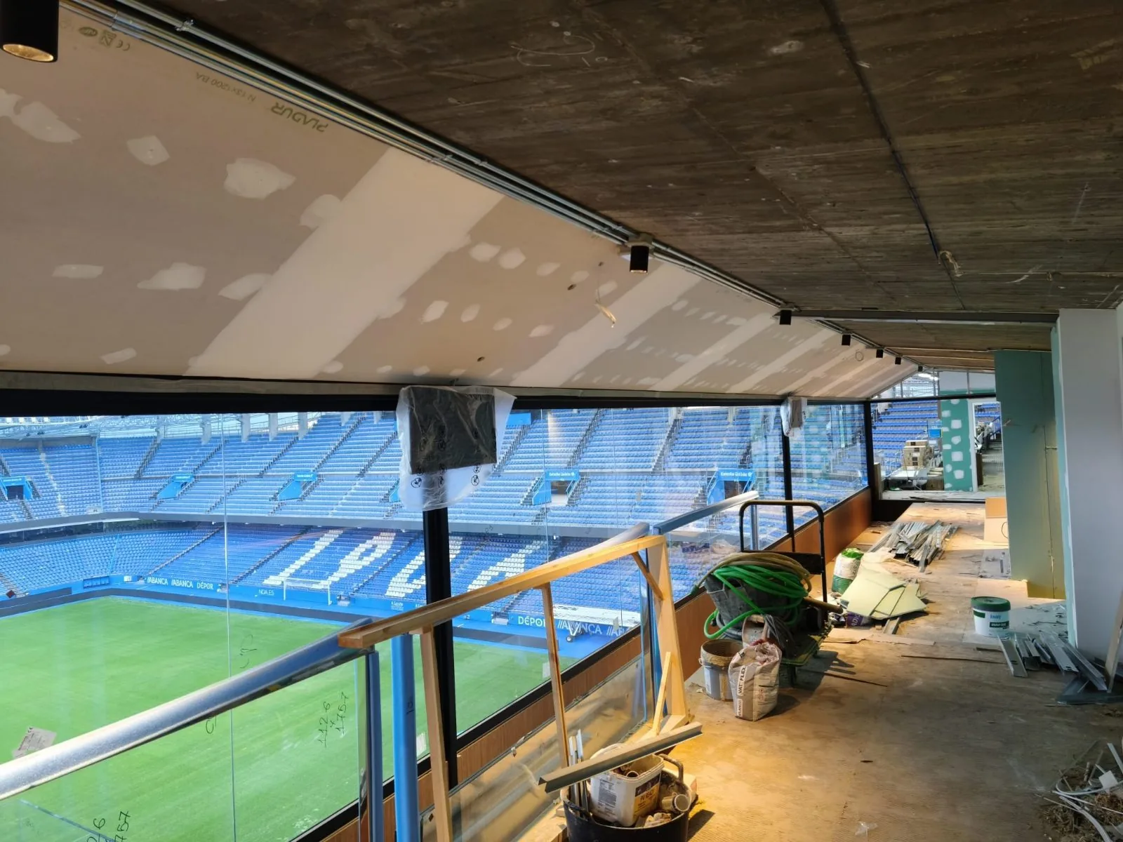 Palco de estadio en obra con carril de focos en el techo y vistas al campo