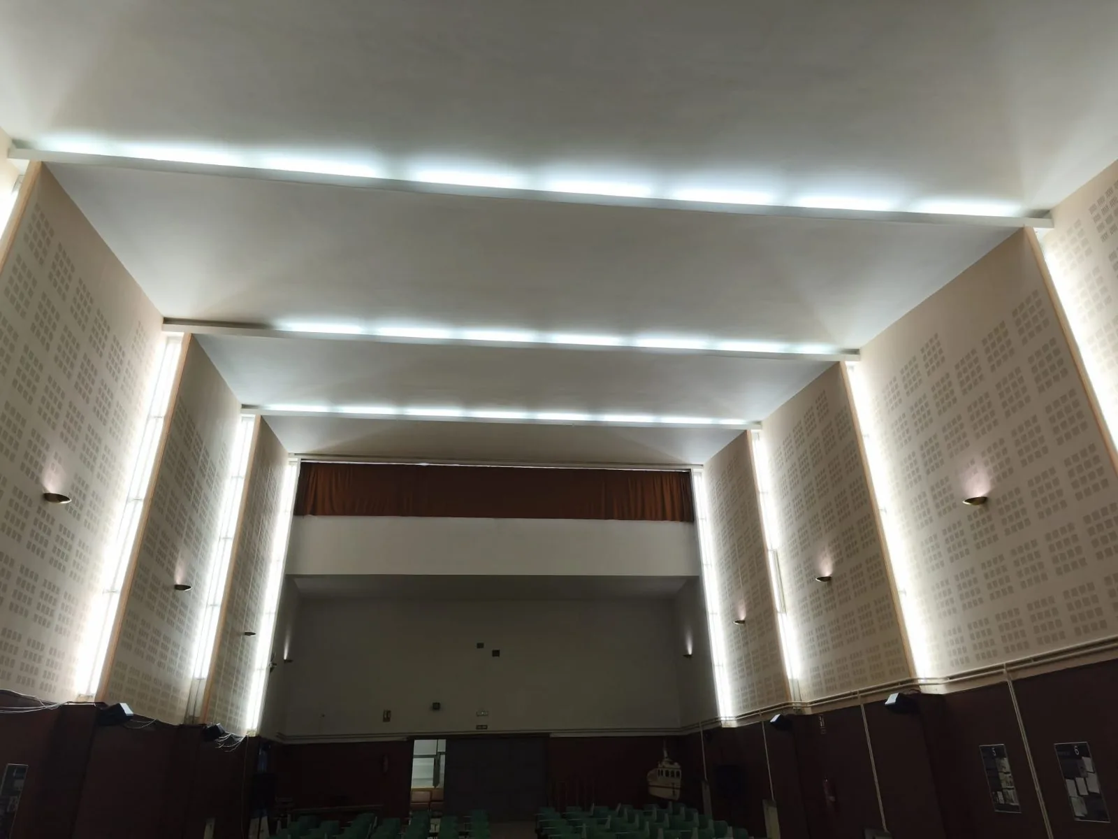 Techo de un salón de actos con líneas de luz LED y apliques en las paredes